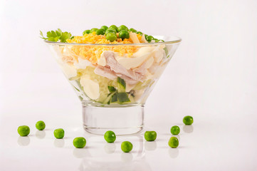 Chicken salad with mayonnaise. With a side dish of cucumber, green peas and boiled egg yolk. Served portion in glassware. Close up and horizontal view.