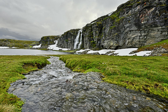 Water stream joying Flotvatnet lake, rocky wall and the waterfall are at background.Norway.