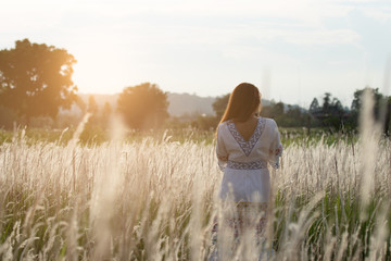 Naklejka na ściany i meble Long haired woman wearing a white dress standing in a field of white grass