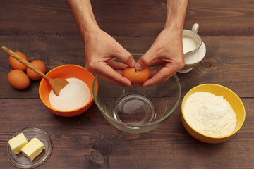 Obraz na płótnie Canvas Cook hands break an egg over a bowl on a wooden table.