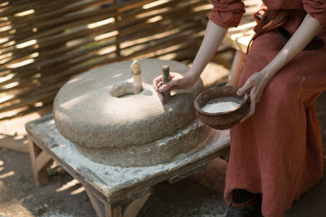 Woman grinds wheat and makes flour on millstone - obrazy, fototapety, plakaty