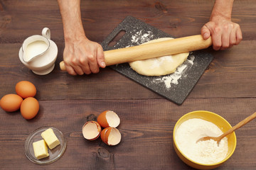 Cook rolling dough with rolling pin on the board on a rustic table.