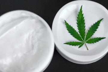 Close up of jar of cream from biological and ecological plants of hemp vegetable pharmaceutical oil CBD with green cannabis leaf with copy space