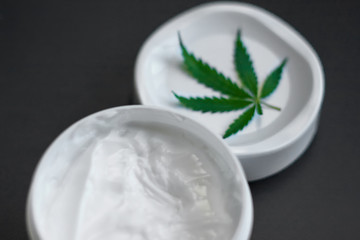 Close up of jar of cream from biological and ecological plants of hemp vegetable pharmaceutical oil CBD with green cannabis leaf with copy space