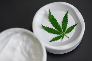 Close up of jar of cream from biological and ecological plants of hemp vegetable pharmaceutical oil CBD with green cannabis leaf with copy space