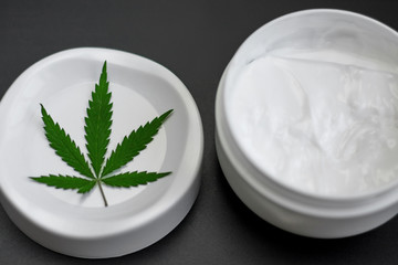 Close up of jar of cream from biological and ecological plants of hemp vegetable pharmaceutical oil CBD with green cannabis leaf with copy space