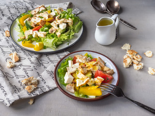 Caesar salad on two plates, large and small, jug with sauce and decorative linen napkin.