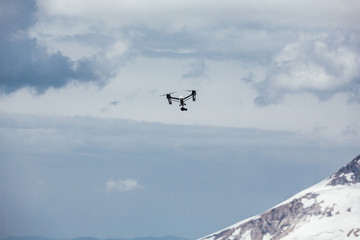 Helicopter flies in the middle of high snow-covered mountains and white cumulus clouds. The concept of tourism in ski resorts and shooting in remote places