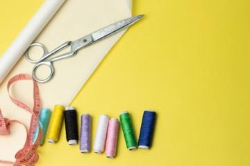 Sewing accessories and fabric on a yelow background. Sewing threads, pins, pattern and sewing centimeter. For sewing at home.Top view, flatlay