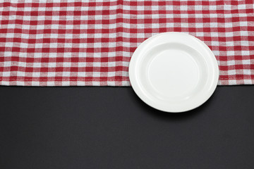 Red and white checkered tablecloth with white empty plate on black dining table