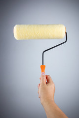 Obraz premium Man holding paint roller on gray background.