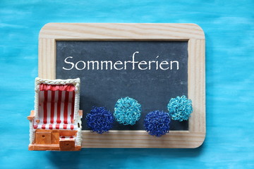Dekoration Sommerferien mit Schieefertafrl und Strandkorb als Symbol für Strandurlaub