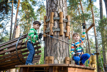 Two little boy boys kid in a helmet and with a safety carbine goes on a rope on the background of forest and sky. Healthy games outdoor