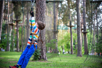 smiling boy rides a zip line. happy child on the zip line. The kid passes the rope obstacle course