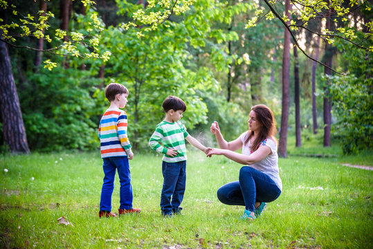 Young Woman Mother Applying Insect Repellent To Her Two Son Before Forest Hike Beautiful Summer Day Or Evening. Protecting Children From Biting Insects At Summer. Active Leisure With Kids