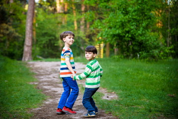 childhood, hiking, family, friendship and people concept - two happy kids walking along forest path