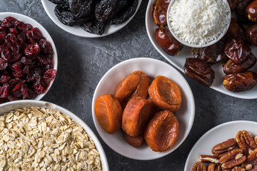 Ingredients for preparing Healthy organic energy balls- dates, dried apricot, oat flakes, raisin, dried cranberries, pecan nuts, coconut shavings on gray background.
