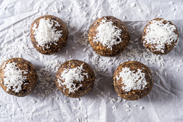 Healthy organic energy balls made with dates, prunes, raisins, peanut, oat flakes, dried cranberries, pecan nuts, coconut shavings, on white cooking paper background.