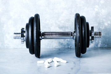 Black heavy dumbbell and creatine capsules on rustic background. Fitness or bodybuilding background  Copy space. 