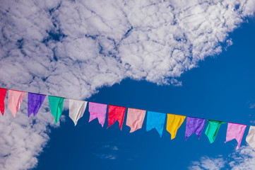cordão de bandeirinhas coloridas com nuvens recortando o céu azul