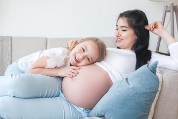 Young pregnant mother and her little daughter indoors. Child and her mom waiting for a little new born baby. Happy family expecting.