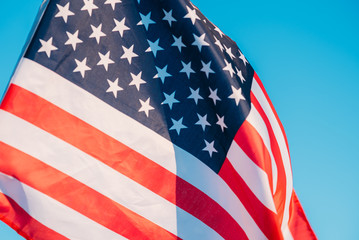 Fototapeta premium American flag in a blue sky, close up. Symbol of Independence Day fourth of July in USA