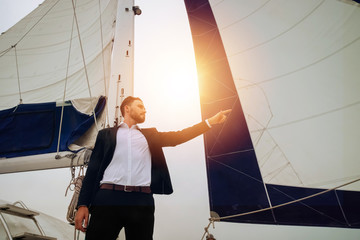 Young handsome and confident Caucasian businessman pointing finger forward on sailing yacht boat...