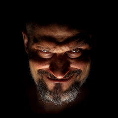 Comedic, fabulous villain or negative character. Face with a bearded man grimace against a dark background with sharp shadows.