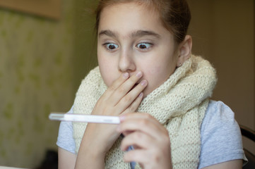little girl in a room in a scarf with a throat wound with a temperature and a thermometer, sneezing...