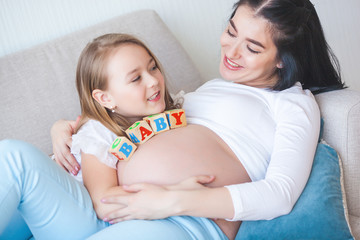 Young pregnant mother and her little daughter indoors. Child and her mom waiting for a little new born baby. Happy family expecting.
