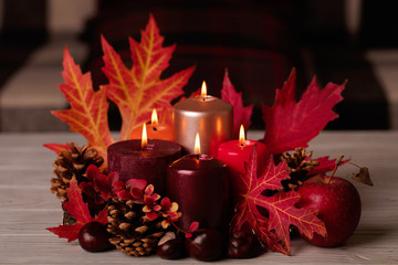 Autumn still life - candles, leaves and cones on the background of pillows.