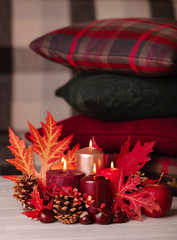 Autumn still life - candles, leaves and cones on the background of pillows.