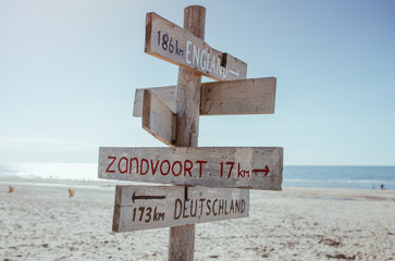 Wooden information board with distance to England, Germany and Zandvoort on the beach by the North Sea in Noordwijk, The Netherlands - obrazy, fototapety, plakaty