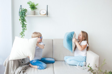 Cute little kids playing with pillows indoors. Brother and sister having fun together. Pillow fight.