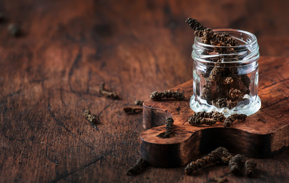 Fragrant long pepper spilling out of glass jar, vintage kitchen table background, selective focus
