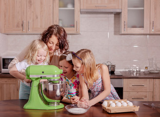Large family - a mother and three children - two daughters and a son, cook in the kitchen, whip the cream in a blender.