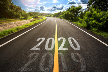 The word 2020 written on highway road in the middle of empty asphalt road at golden sunset and...
