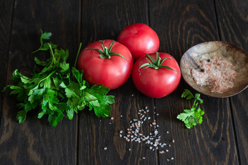 Fresh tomatoes with parsley and salt on a dark wooden background. Copy space. Harvesting tomatoes. 