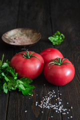 Fresh tomatoes with parsley and salt on a dark wooden background. Copy space. Harvesting tomatoes. 