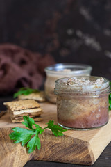 Obraz na płótnie Canvas Fresh homemade liver pate in a glass jar with multigrain crackers and parsley on a wooden background.