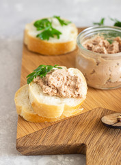 Obraz na płótnie Canvas Liver pate in a glass jar with fresh bread and parsley on a wooden cutting board. Light grey stone background.
