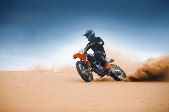 Rider on a cross-country enduro motorcycle go fast at the desert. Enduro racing driver take a corner with a splashes of sands and dust