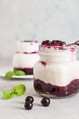 Jars of natural yogurt with berry sauce and mint on light grey table. Healthy eating. Copy space. Summer food concept. 