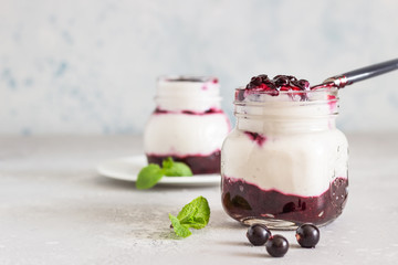 Jars of natural yogurt with berry sauce and mint on light grey table. Healthy eating. Copy space. Summer food concept. 