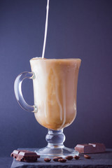 Iced coffee with milk on a dark background. Latte and black chocolate on a slate board. Milk drink in a glass, and coffee beans. Copy space