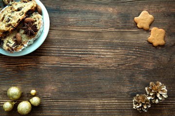 Traditional Christmas cake pieces and gingerbread cookies on brown rustic table. Space for text, free space. Golden cones and golden Christmas balls decorations. 