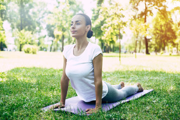 Beautiful young woman doing yoga at park and looking away. Brunette woman enjoying nature during a...