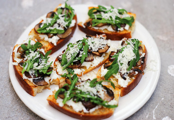 Homemade bruschetta with mozzarella, mushrooms and arugula in a plate closeup