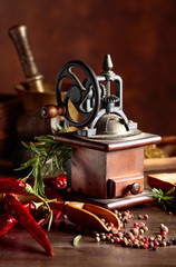 Vintage pepper mill with kitchen utensils, spices and rosemary on a old wooden table.