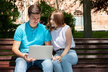 Happy young couple using laptop computer sitting on bench in city outdoor - Concept of relationship and people addicted to technology